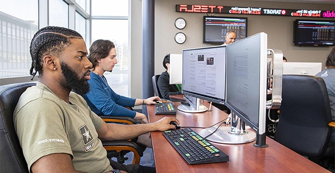 Students and professor in finance lab with computers and ticker